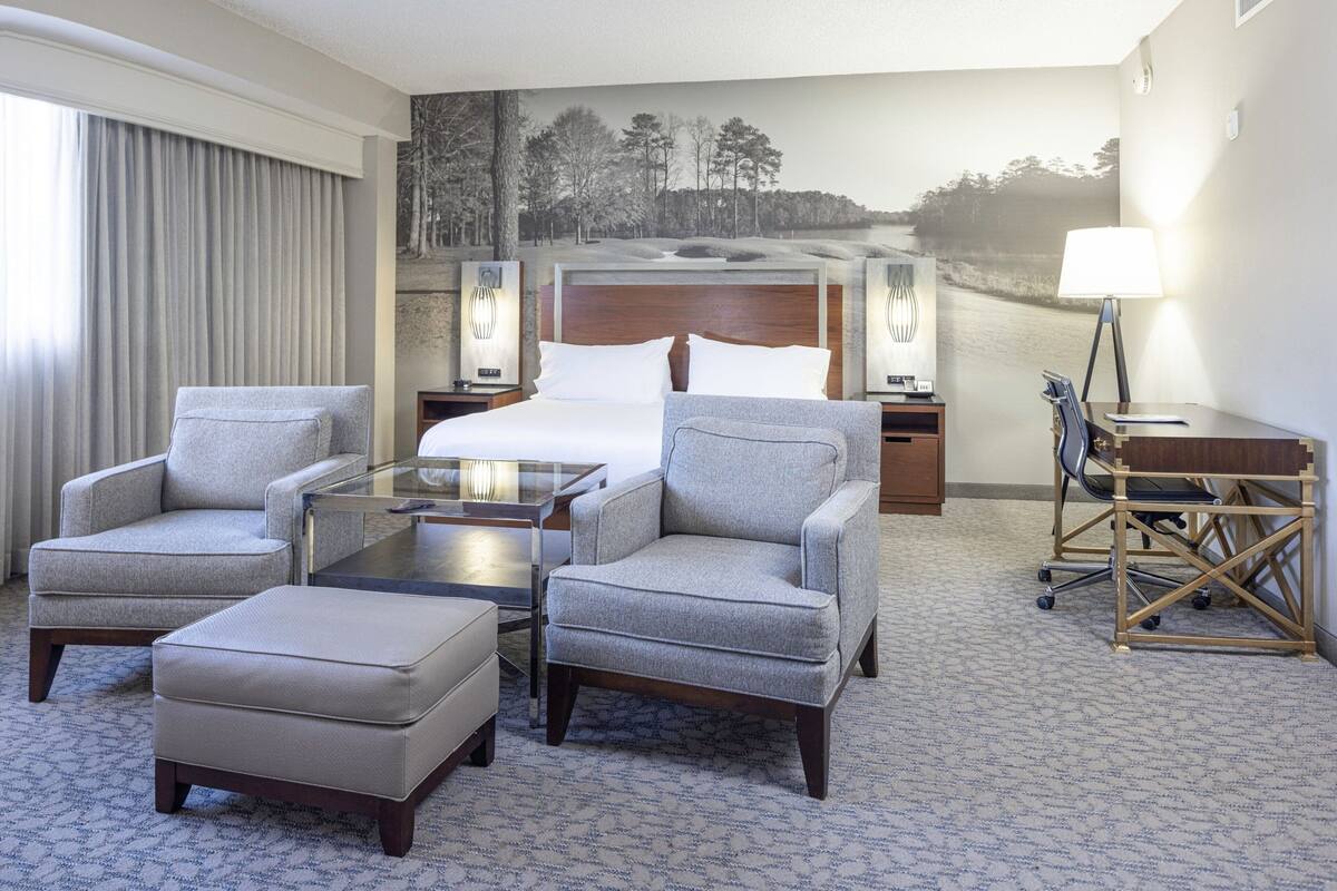Ein Hotelzimmer mit einem großen Bett, zwei Sesseln, einem kleinen Tisch, einem Schreibtisch und einem Stuhl.