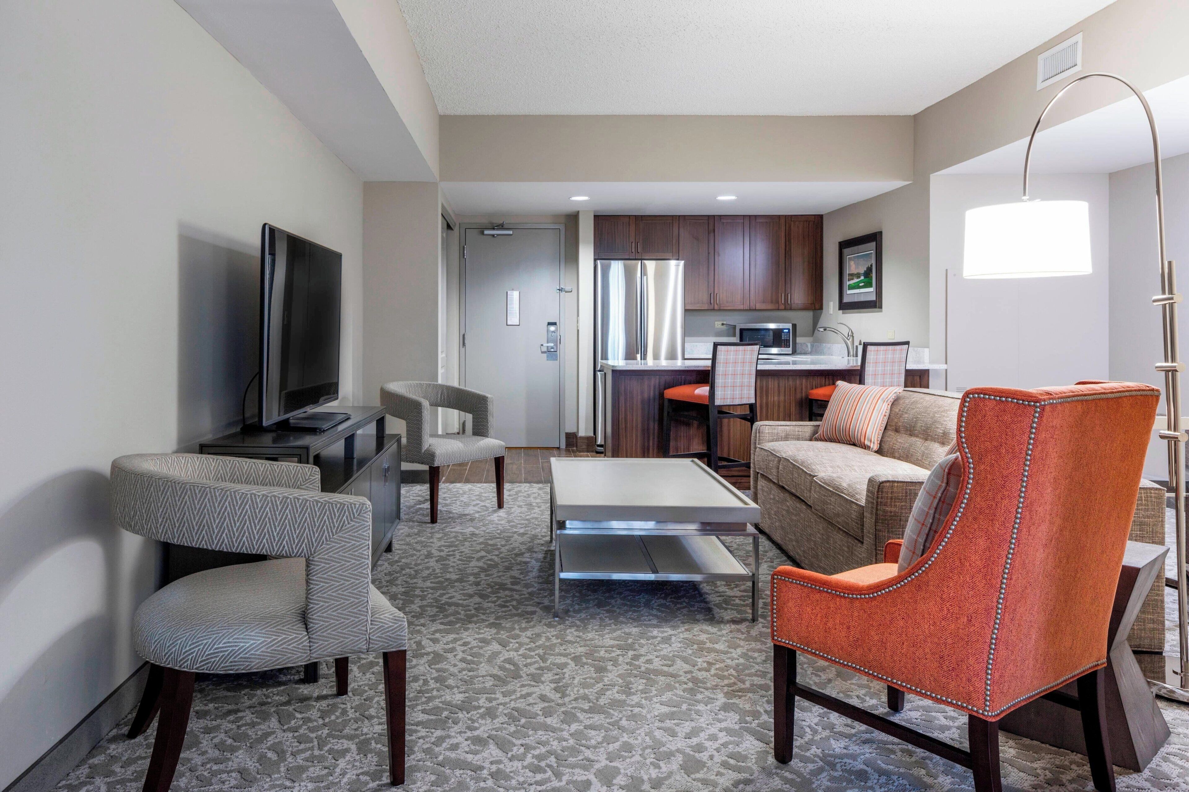 A hotel room with a living area, kitchenette, and a television.