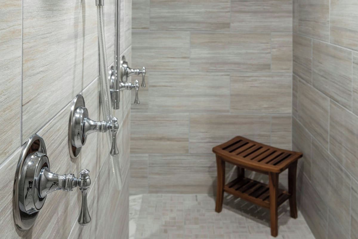 Ein modernes Badezimmer mit Dusche, einem Holzschemel und einer gefliesten Wand.