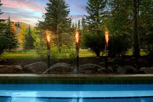 A pool area with a fountain and three torches in a landscaped garden.