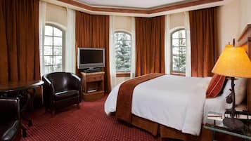A hotel room with a bed, a desk, a chair, a television, and a lamp.