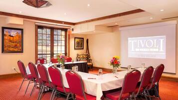 A conference room with a projection screen displaying 'TIVOLI IN VAIL VILLAGE', red chairs, a table with a white tablecloth, and framed artwork on the walls.