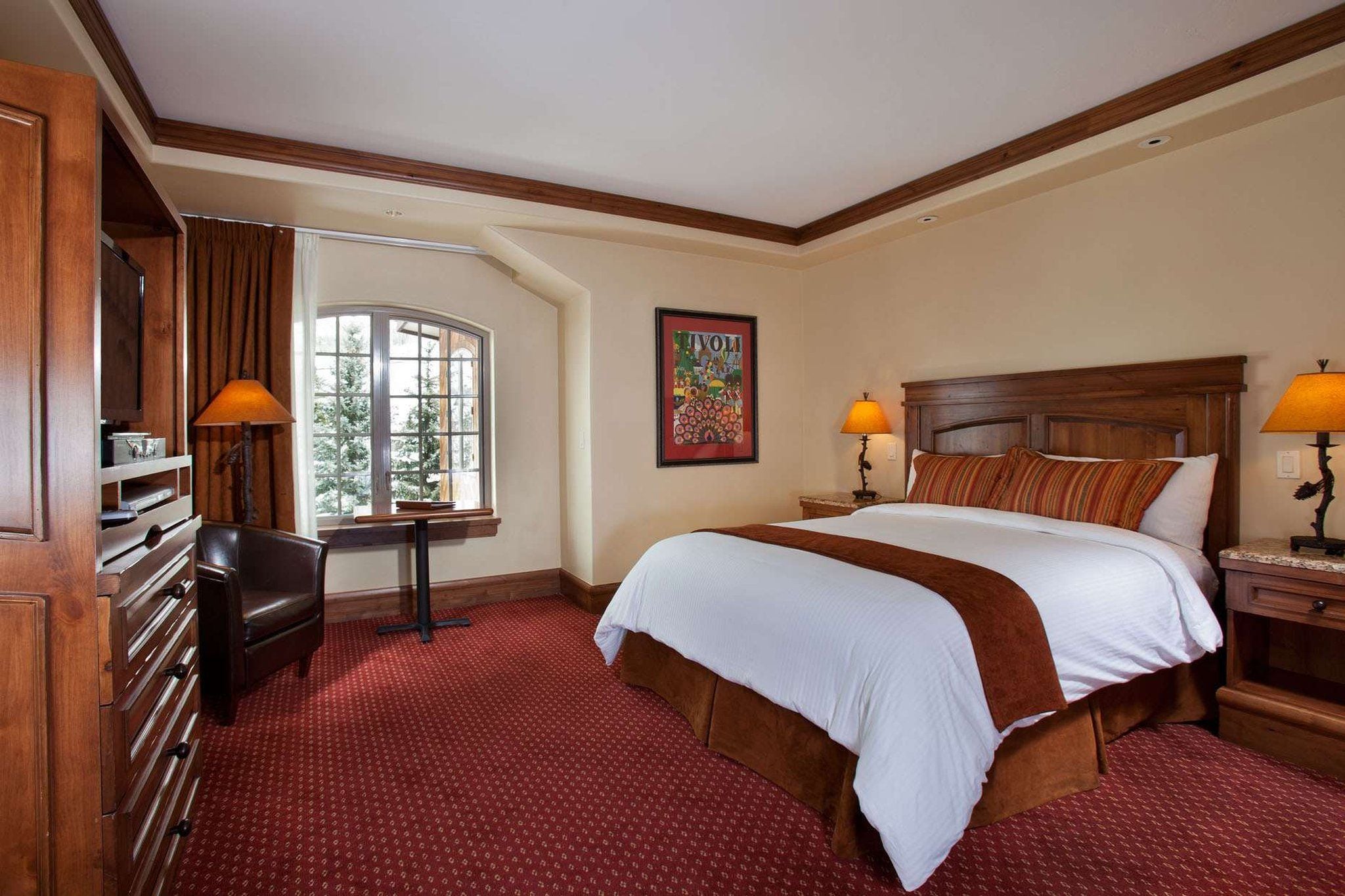 A hotel room with a large bed, a desk, a chair, a window, and a painting on the wall.