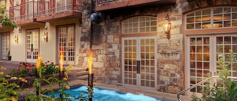 A hotel with a stone facade, a swimming pool, and a balcony with a wrought iron railing.