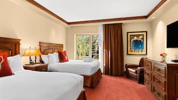 A hotel room with two beds, a wooden headboard, a desk with drawers, a television, and a window with curtains.