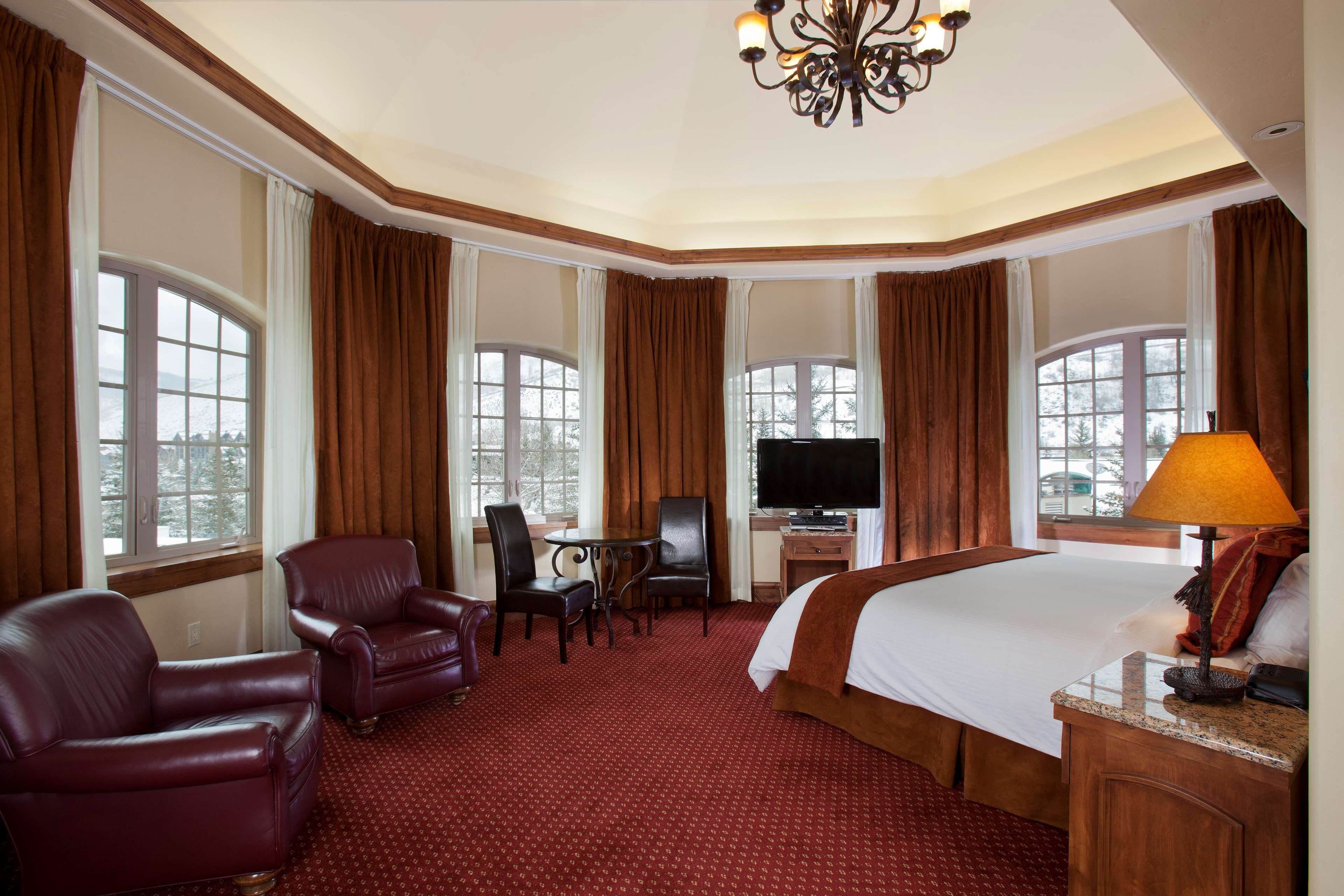 A hotel room with a large bed, a TV, a desk, and leather chairs.