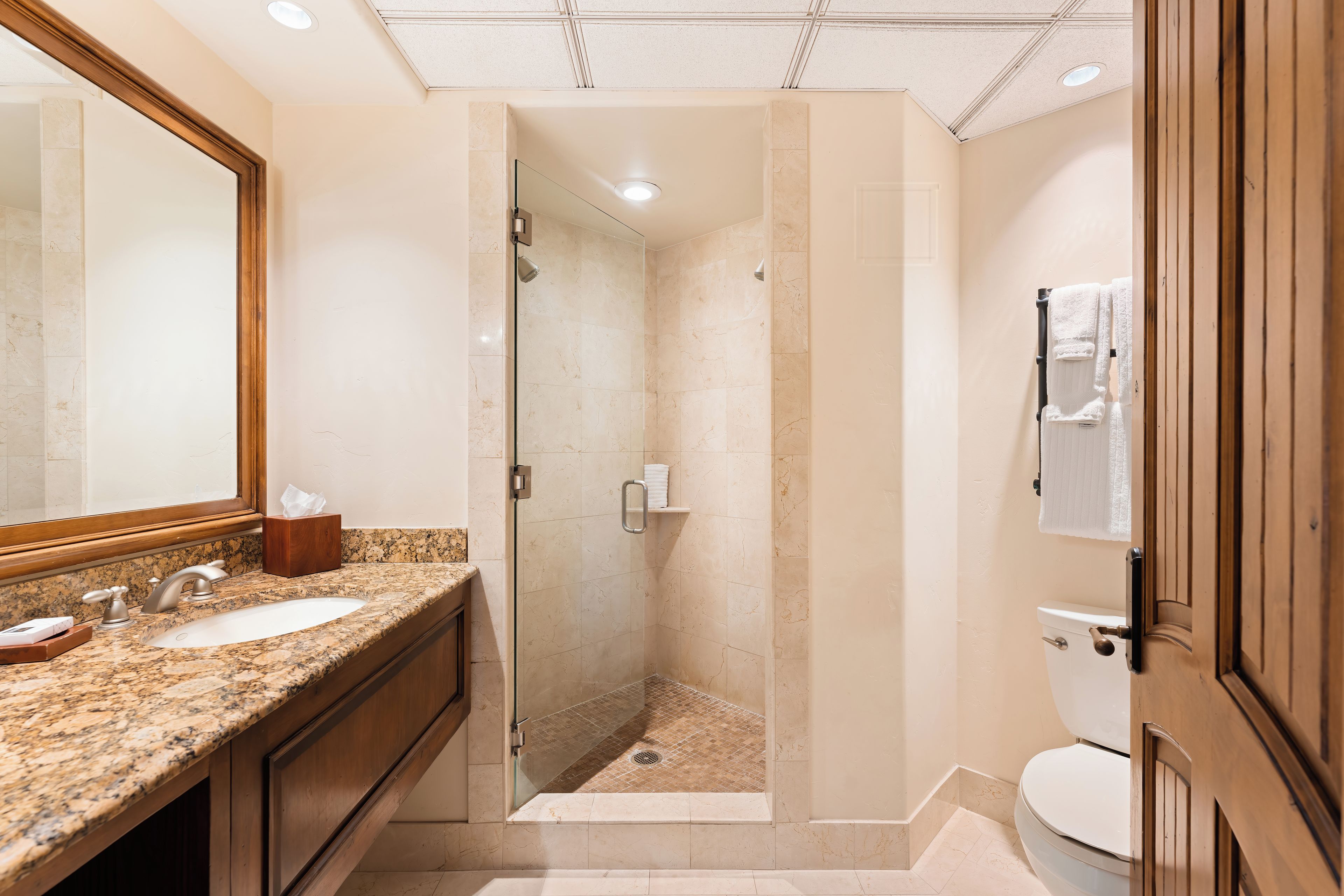 A bathroom with two sinks, a glass-enclosed shower, and a toilet.