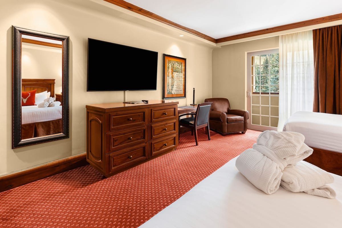 A hotel room with a bed, a desk with a chair, a television, a dresser, and a large mirror.