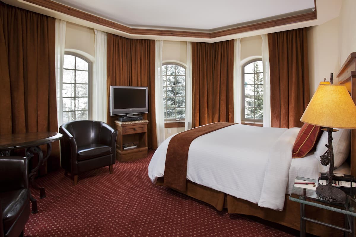 A hotel room with a large bed, a television, a desk with a chair, and a lamp.