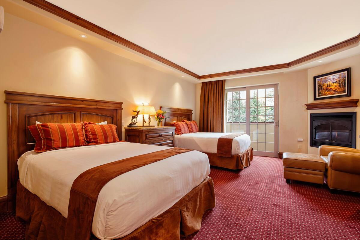 A hotel room with two beds, a fireplace, a sofa, and a large window.