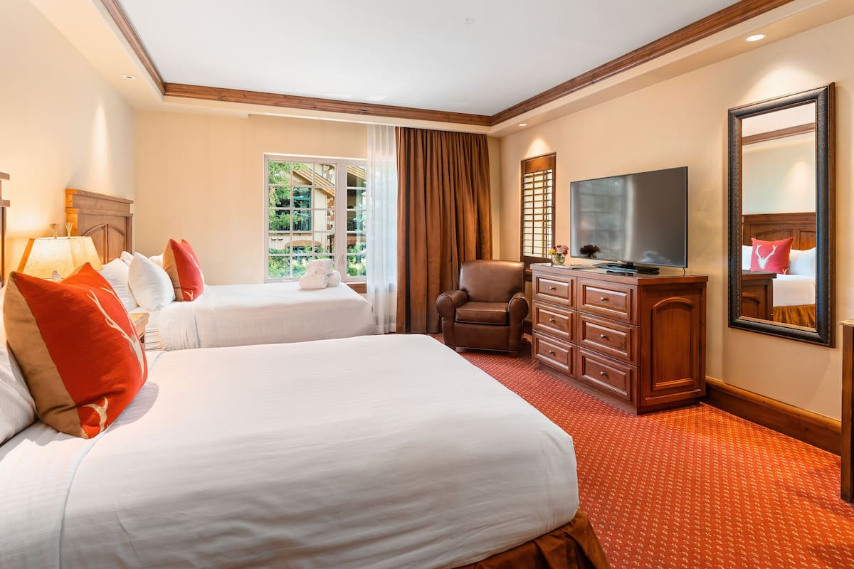A hotel room with two beds, a TV, a chair, and a dresser.