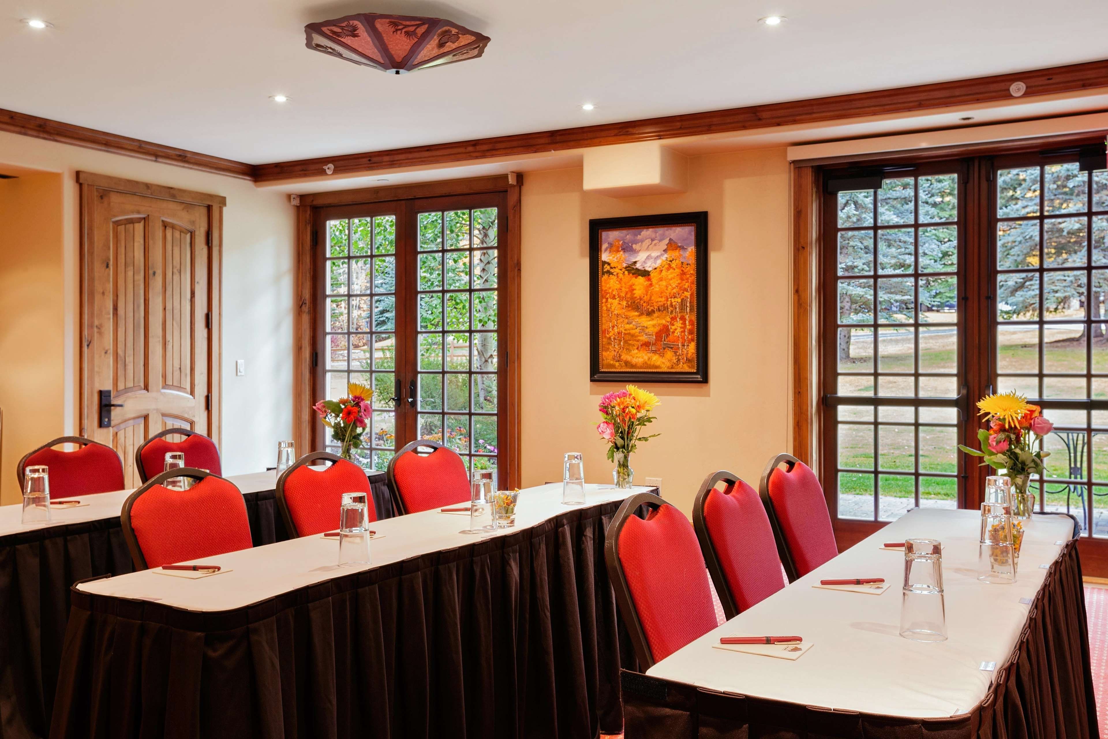 Ein Konferenzraum mit einem langen Tisch, roten Stühlen und großen Fenstern mit Blick auf Bäume.