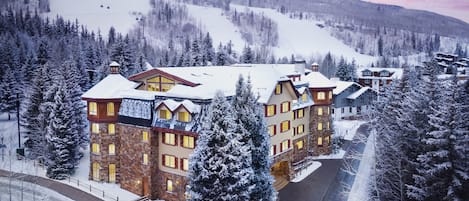 A multi-story hotel with a stone facade, multiple windows, and a snow-covered landscape in the background.