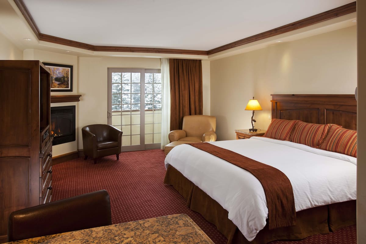 A hotel room with a large bed, a fireplace, a desk, and a view of the outdoors.