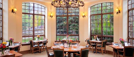 A dining area with round tables, chairs, and a chandelier.