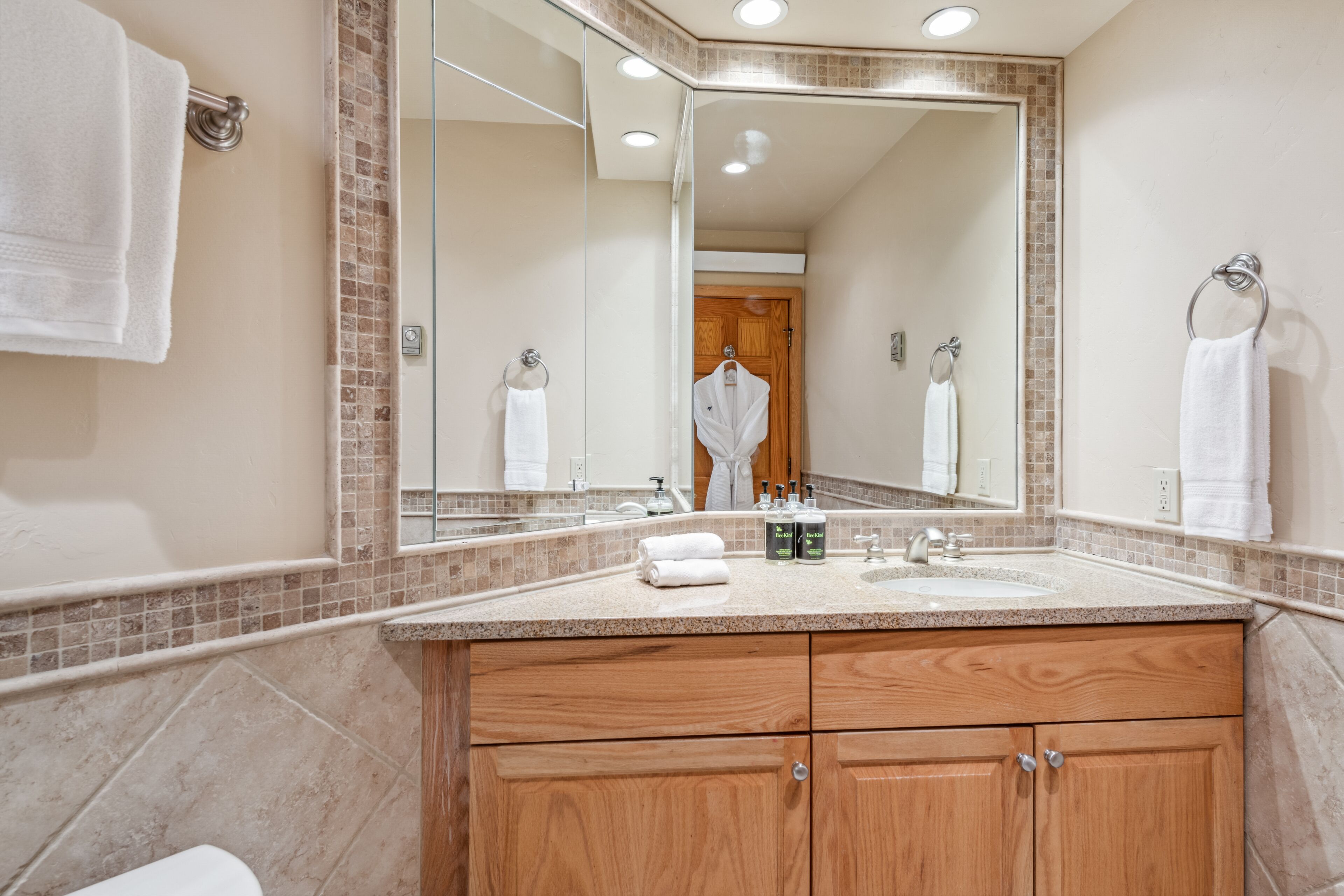 A bathroom with a large mirror, wooden vanity, and a sink with toiletries.