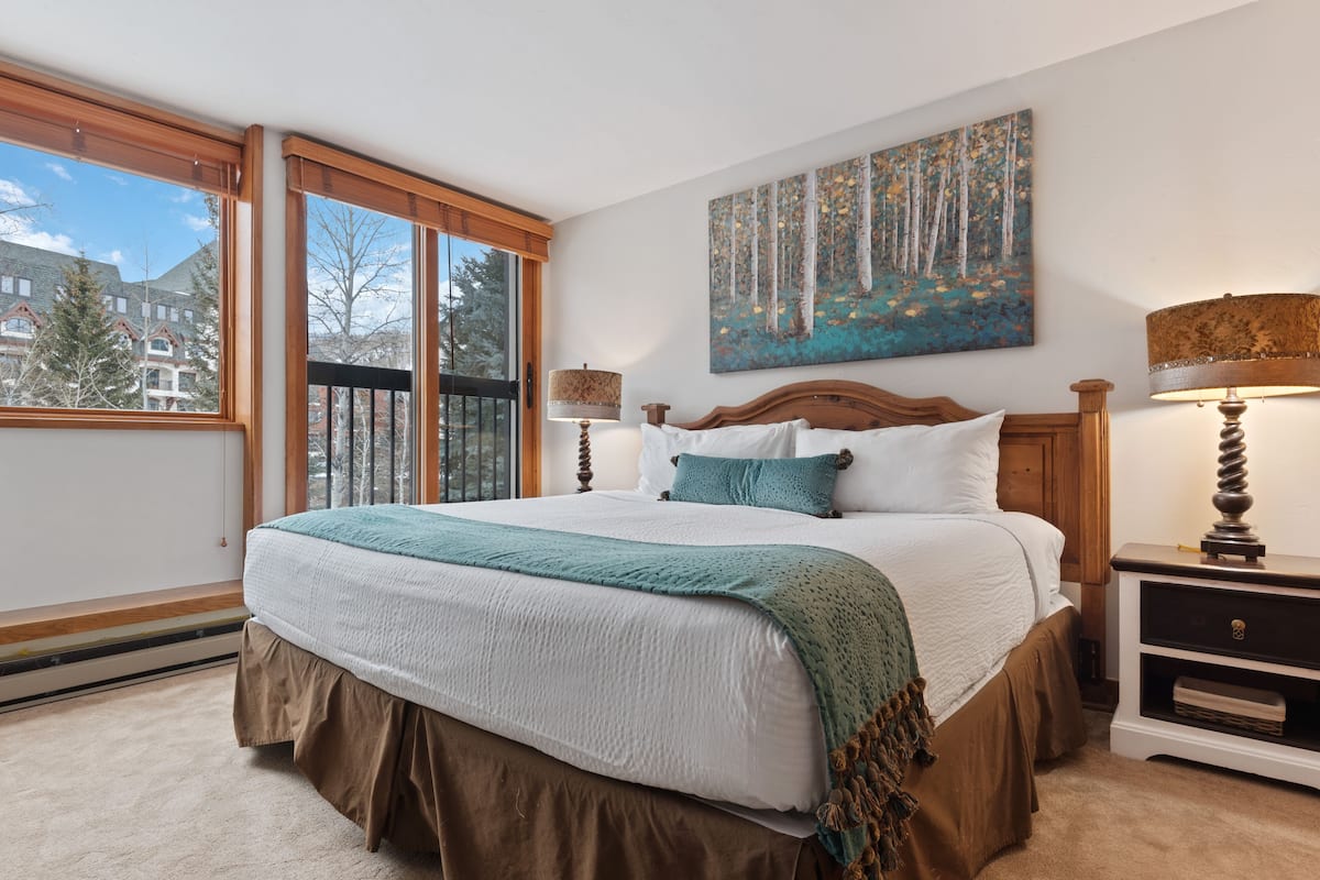 A bedroom with a large bed, two bedside tables, a window, and a painting on the wall.