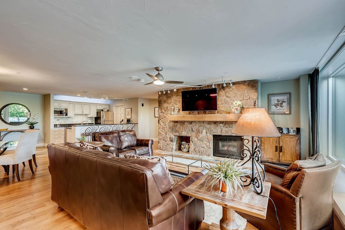 A modern living room with a stone fireplace, leather sofa, and a dining area with a glass table.