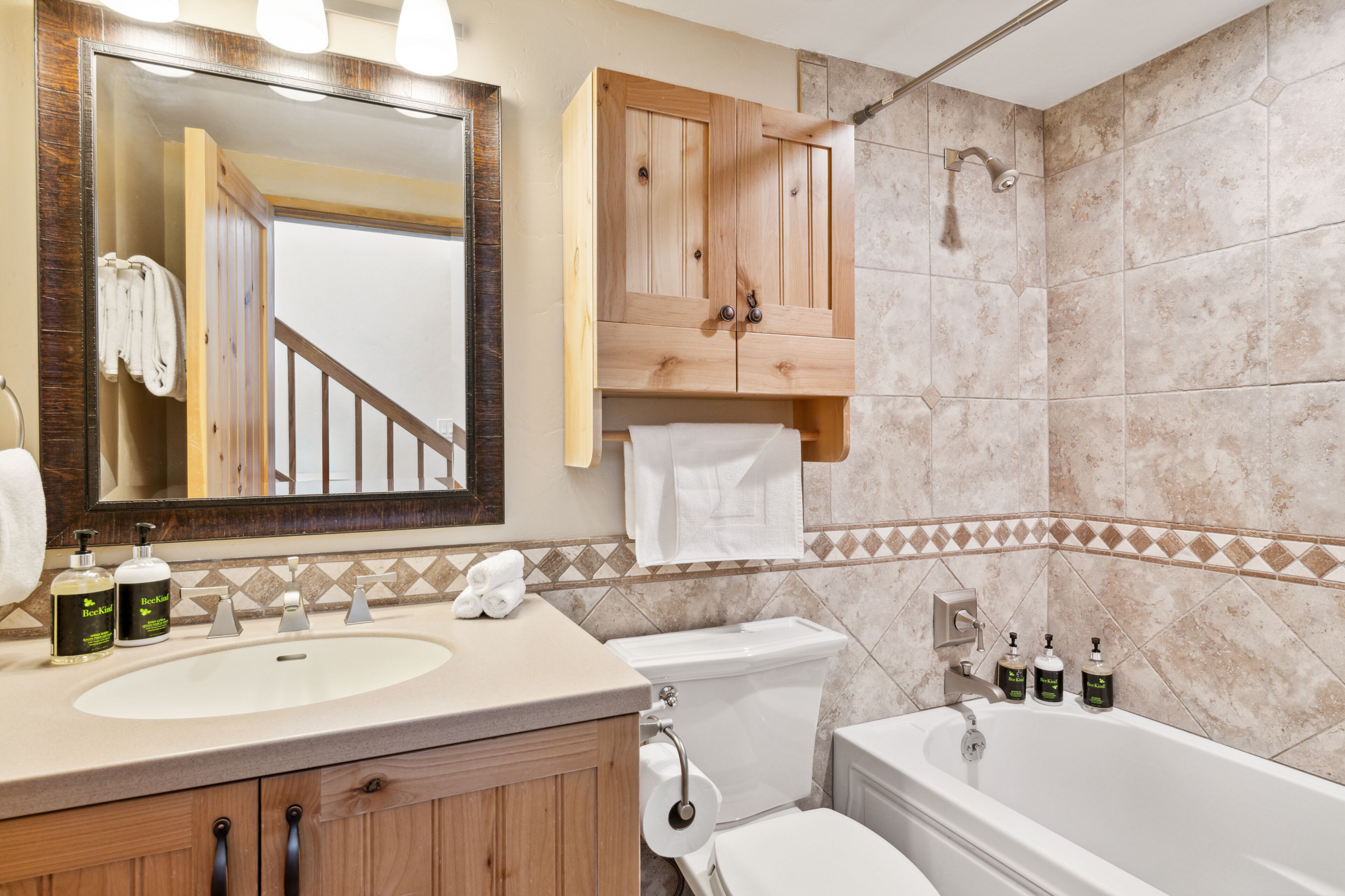 Ein Badezimmer mit Holzwaschtisch, einem großen Spiegel, einer Badewanne und einer Toilette.
