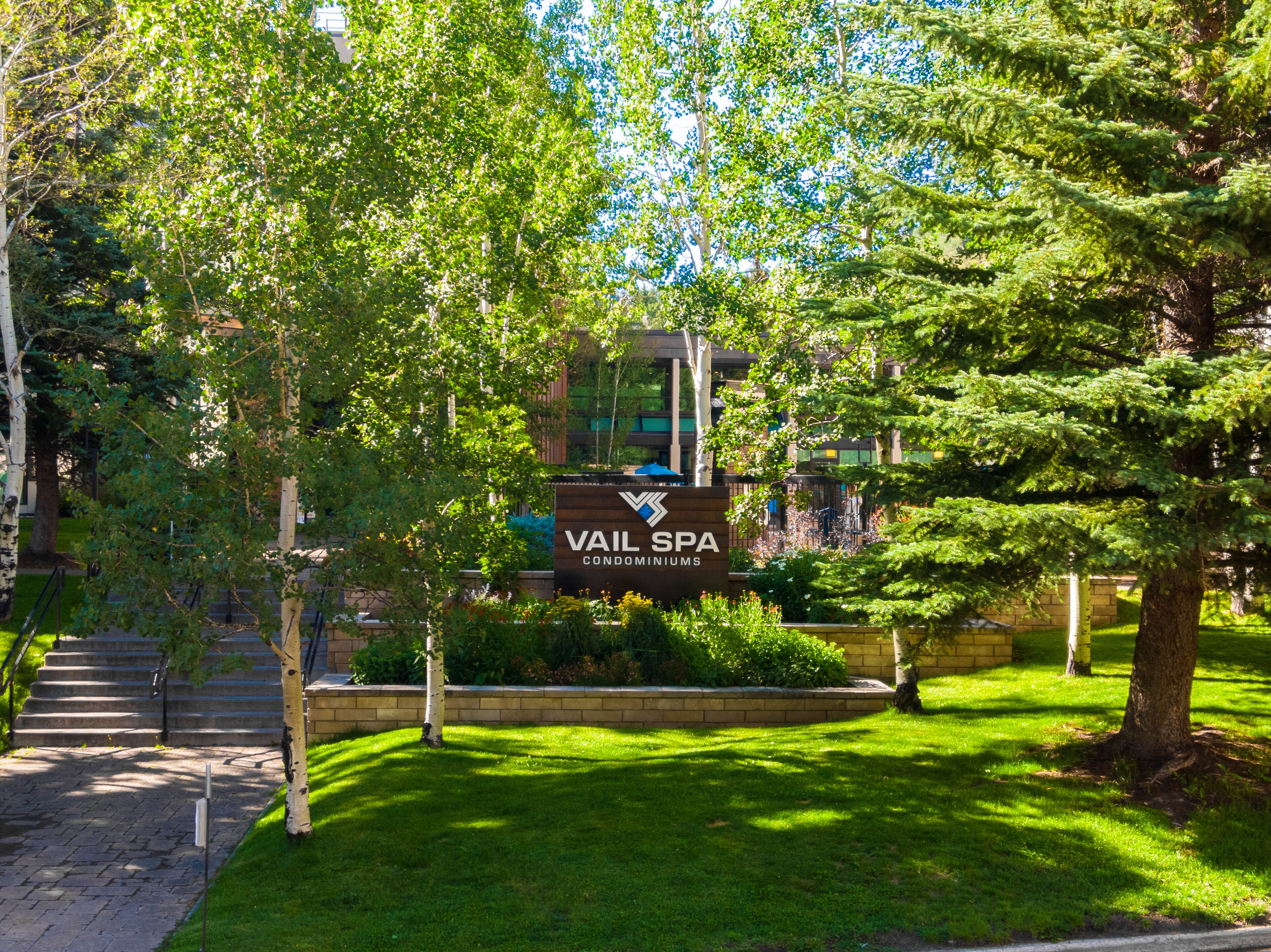 A sign for VAIL SPA Condominiums surrounded by lush greenery and a brick pathway.