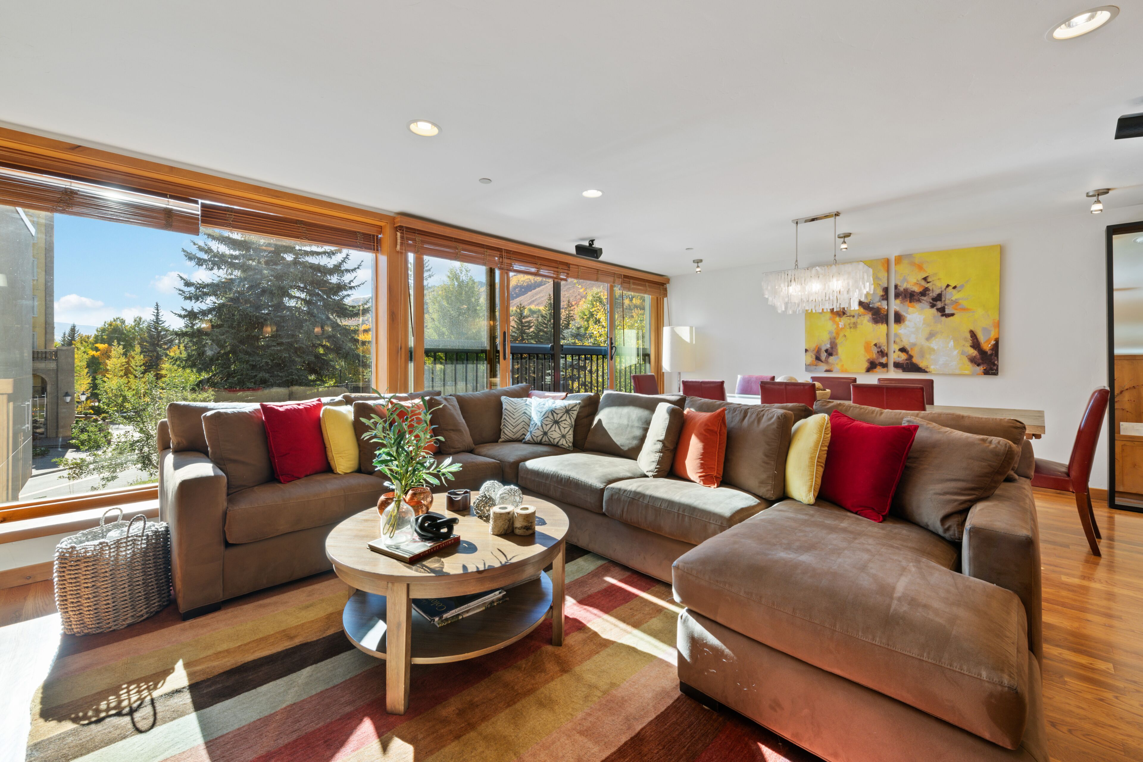 A modern living room with a sectional sofa, a coffee table, and large windows offering a view of trees and mountains.