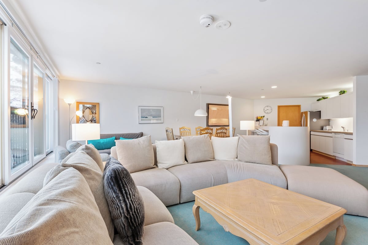 A modern living room with a large sectional sofa, a wooden coffee table, and a kitchen area in the background.