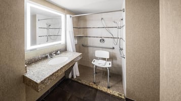 A modern bathroom with a granite countertop sink, a mirror, a shower with a handheld showerhead, and a grab bar.
