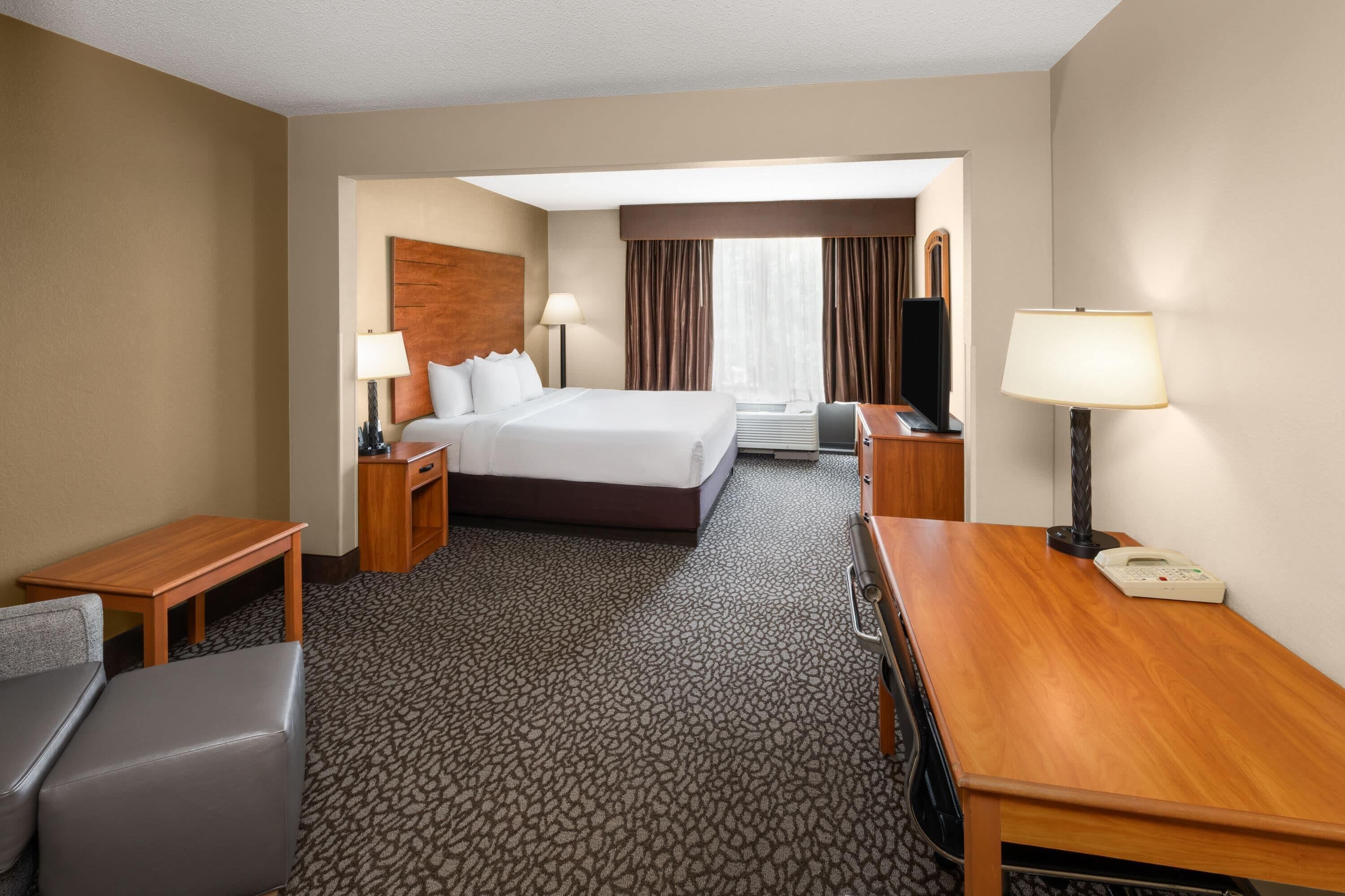 Une chambre d’hôtel avec un grand lit, deux tables de chevet, un bureau, une chaise et un téléphone.