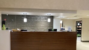 A reception desk with a wooden finish, a black mat with "Wingate by Wyndham" logo, and a textured wall behind. - Wingate by Wyndham Little Rock (Little Rock)