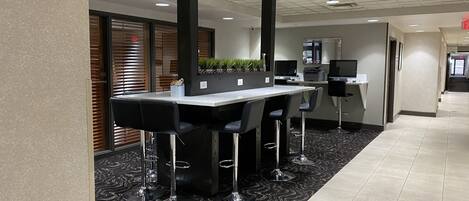 A modern hotel lobby with a reception desk, bar area with stools, and a patterned carpet.
