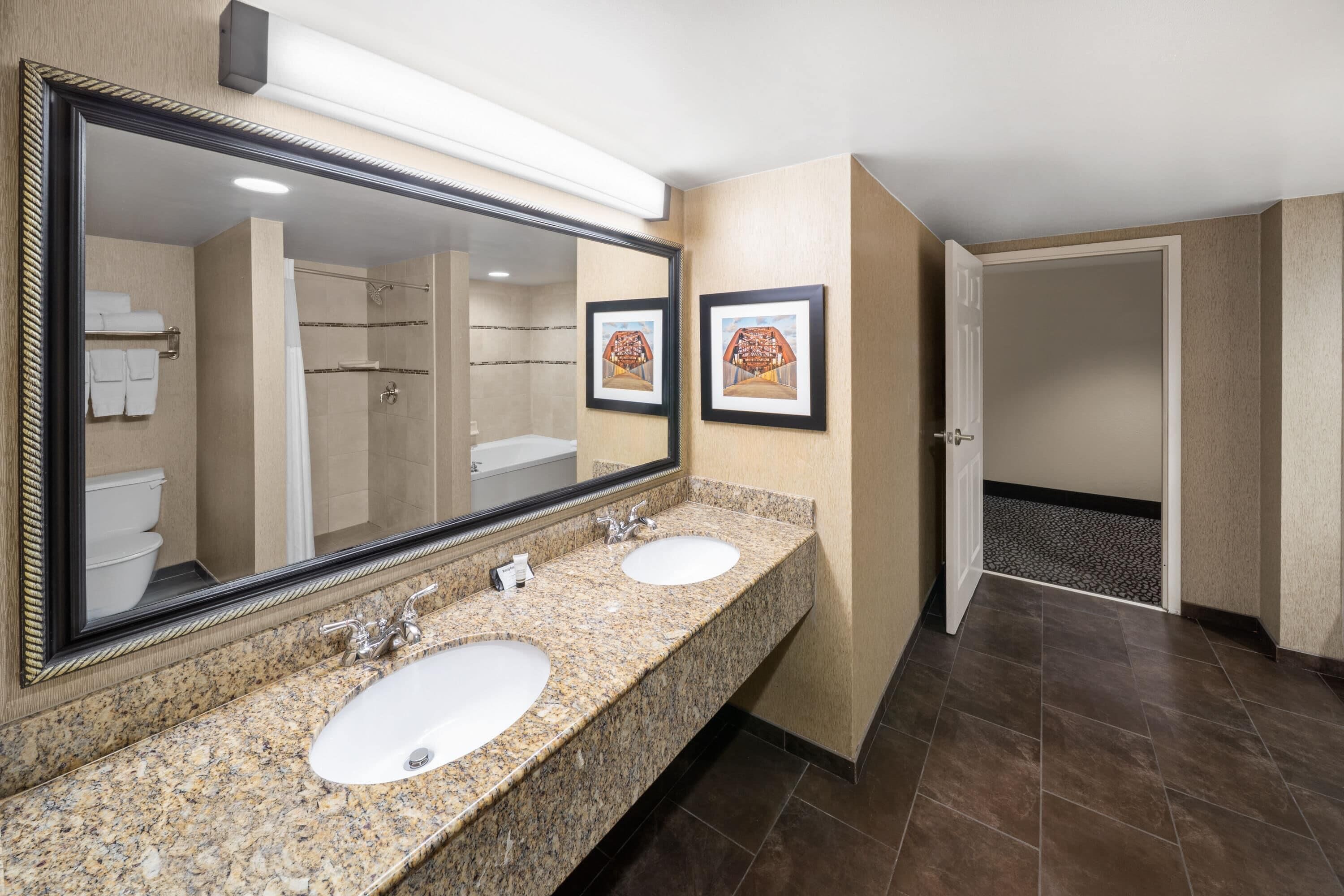 A hotel bathroom with two sinks, a large mirror, and framed artwork on the wall.
