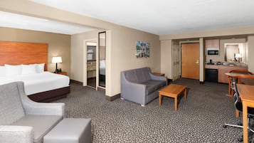 A hotel room with a bed, a sofa, a small table, a desk, and a kitchenette.