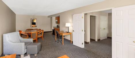 A hotel room with a dining area, a sofa, a desk, and a door leading to another room.