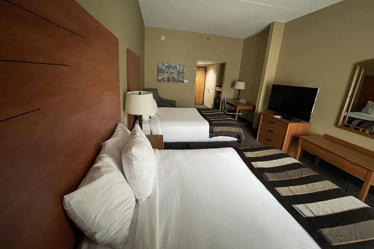 A hotel room with two beds, a TV, a desk, and a mirror.