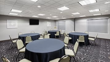 Un salón de conferencias con mesas redondas y sillas, un televisor de pantalla plana y una pantalla de proyección.