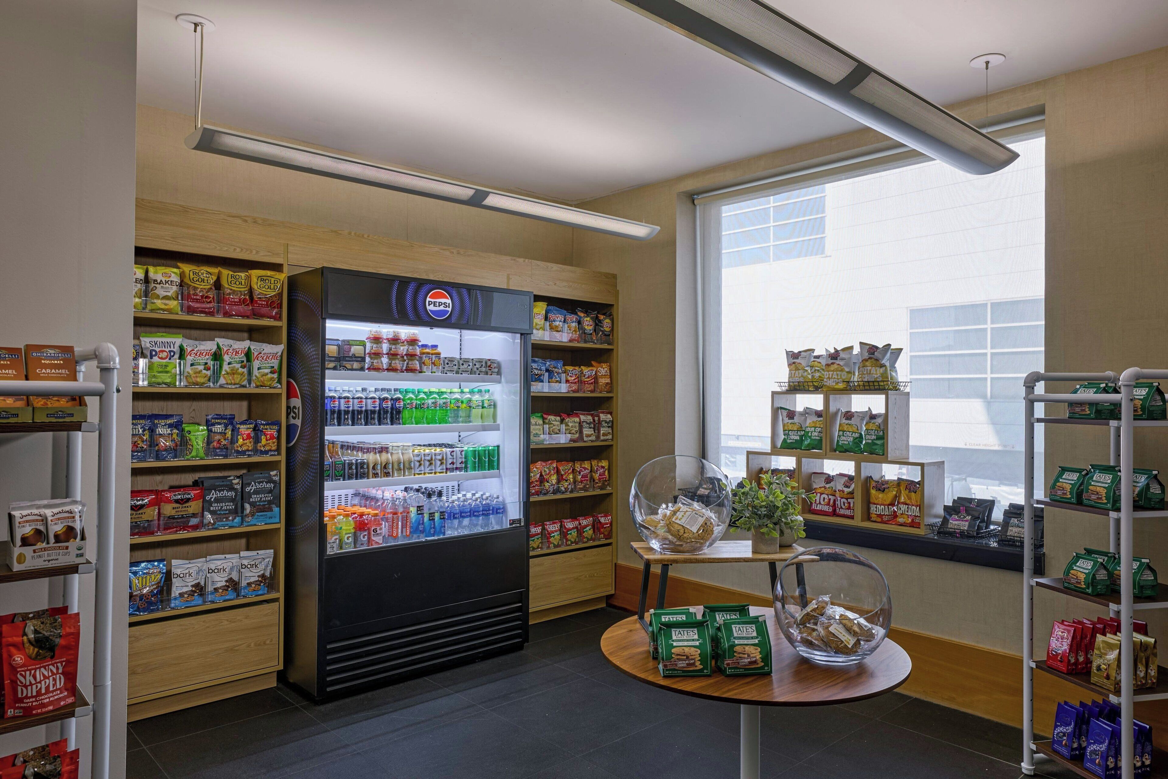 A snack and beverage section with a refrigerated display, shelves stocked with snacks, and a window view.