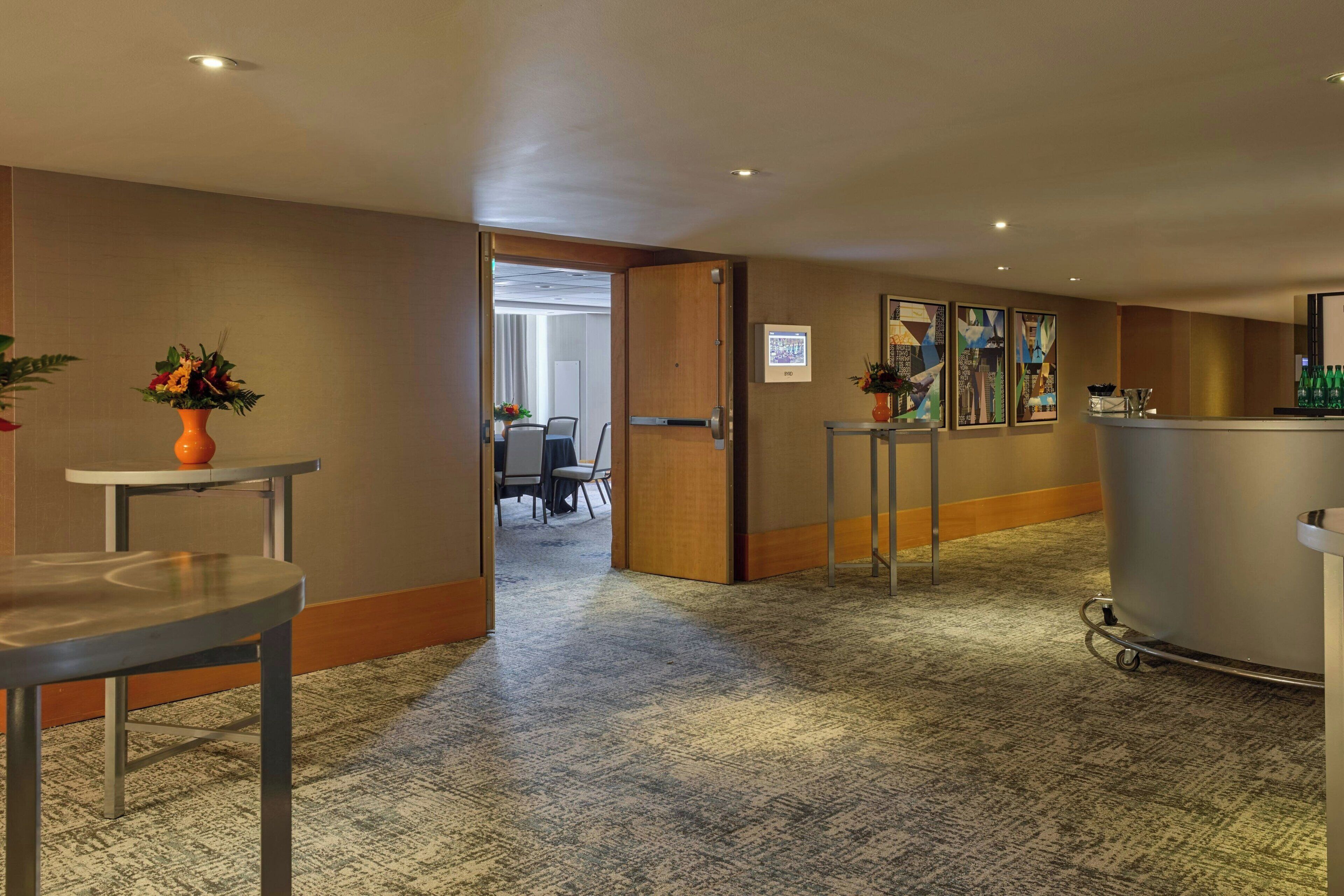 A hotel lobby with a carpeted floor, a reception desk, a seating area with chairs, and framed artwork on the walls.