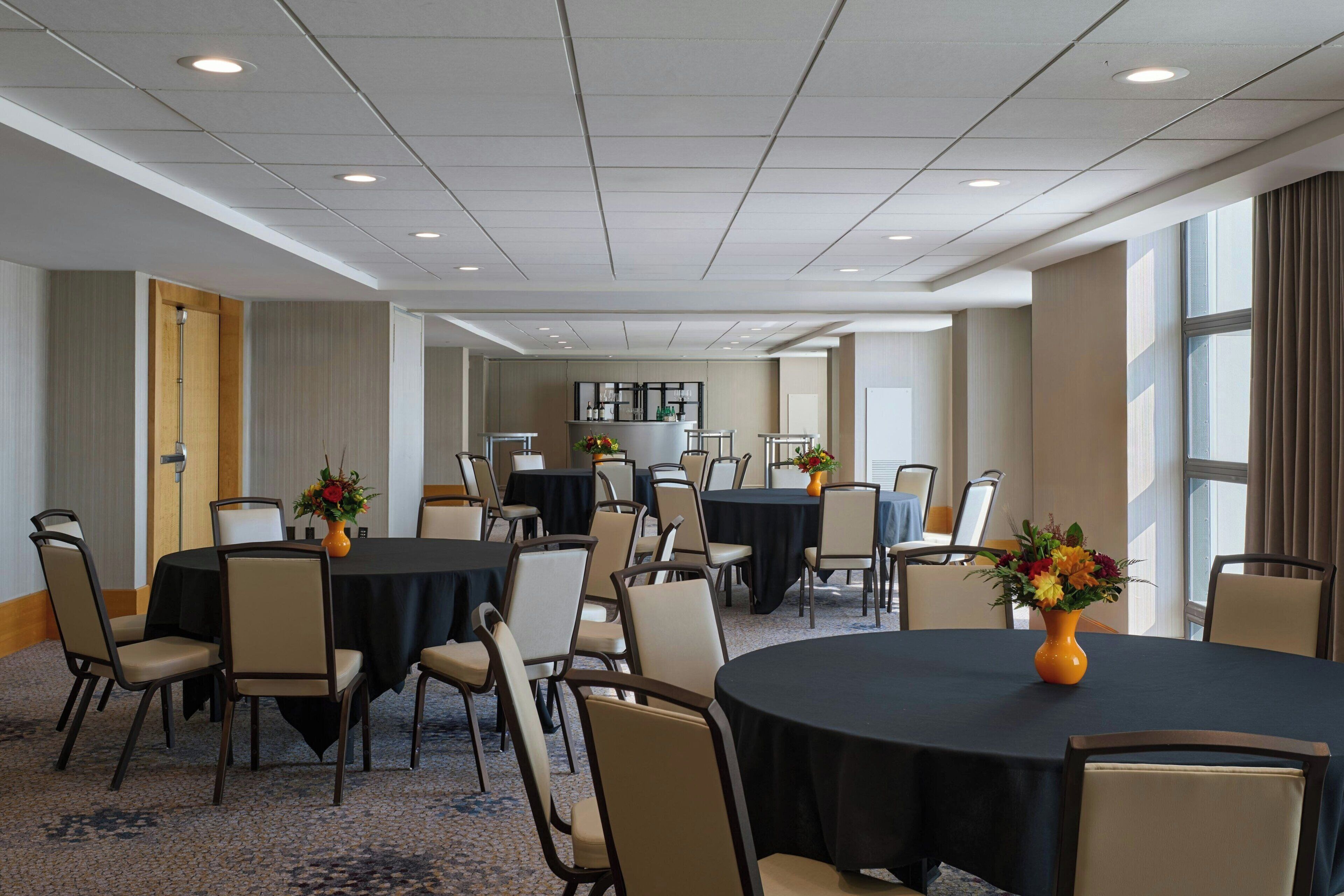 A conference room with multiple tables, chairs, and a central area with a counter and decorative flowers.