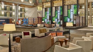 Un hall d’entrée spacieux au design moderne, comprenant un espace détente avec des canapés et des fauteuils, un mur décoratif agrémenté de jardins verticaux et un grand lustre.