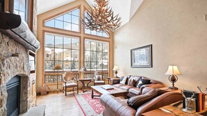 A spacious living room with a fireplace, leather sofa, and large windows offering a view of a snowy landscape. - Oxford Court by East West Hospitality (Avon)