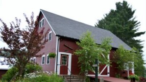 A red brick house with a grey roof, surrounded by a garden with various plants and a stone pathway leading to the front door. - 1824 House (Waitsfield)
