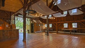A rustic wooden interior with high ceilings, chandeliers, and string lights. - 1824 House (Waitsfield)
