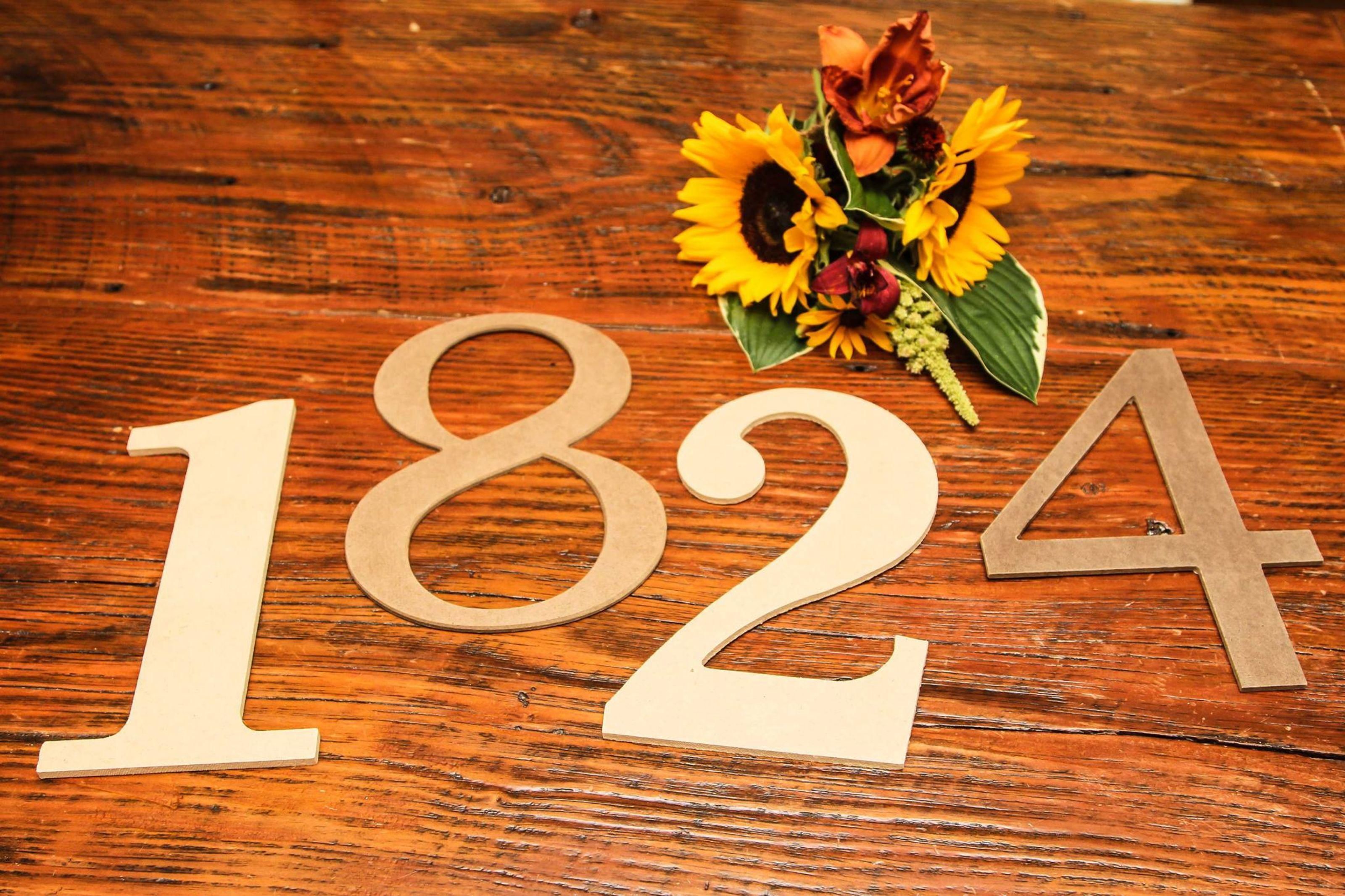 Des chiffres en bois, « 1824 », posés sur une surface en bois, accompagnés d’un bouquet de tournesols.