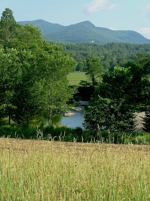 A river flowing through a valley with trees and mountains in the background. - 1824 House (Waitsfield)