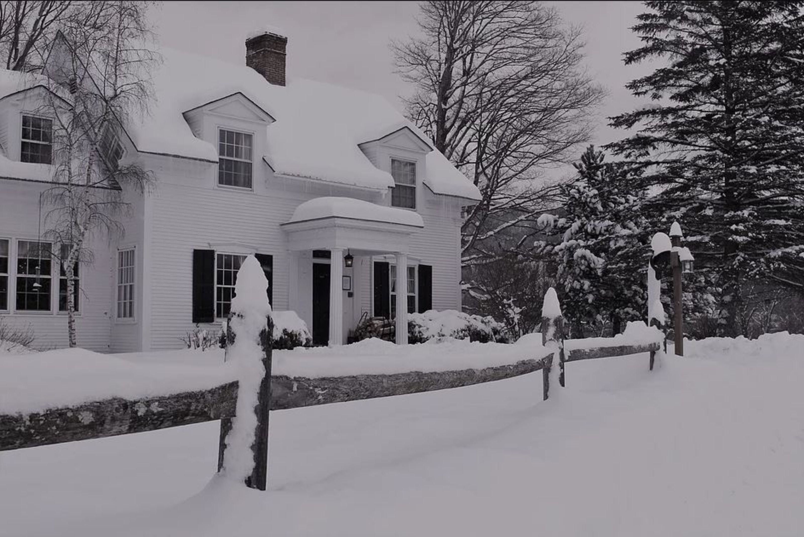 A snow-covered house with a chimney, windows, and a porch.