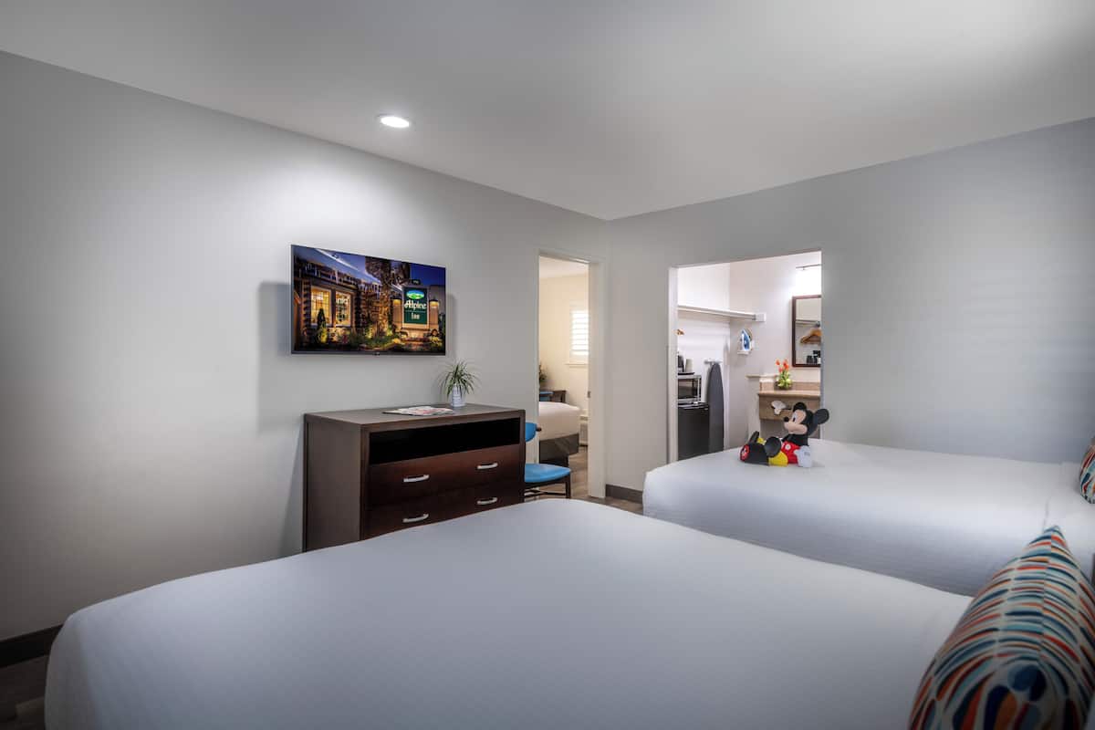 Ein Hotelzimmer mit zwei Betten, einem Schreibtisch mit Schubladen, einem Stuhl, einer Mickey Mouse Figur und einem Bild an der Wand.