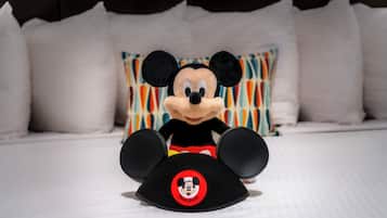 A plush Mickey Mouse toy on a bed with white bedding and colorful pillows.