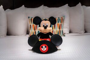 A plush Mickey Mouse toy on a bed with white bedding and colorful pillows.