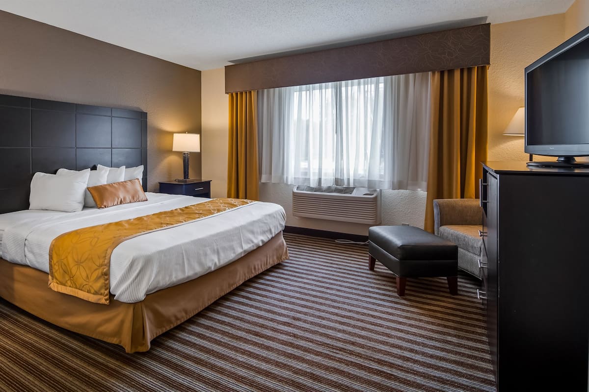 A hotel room with a large bed, a desk, a chair, a television, and a window with curtains.