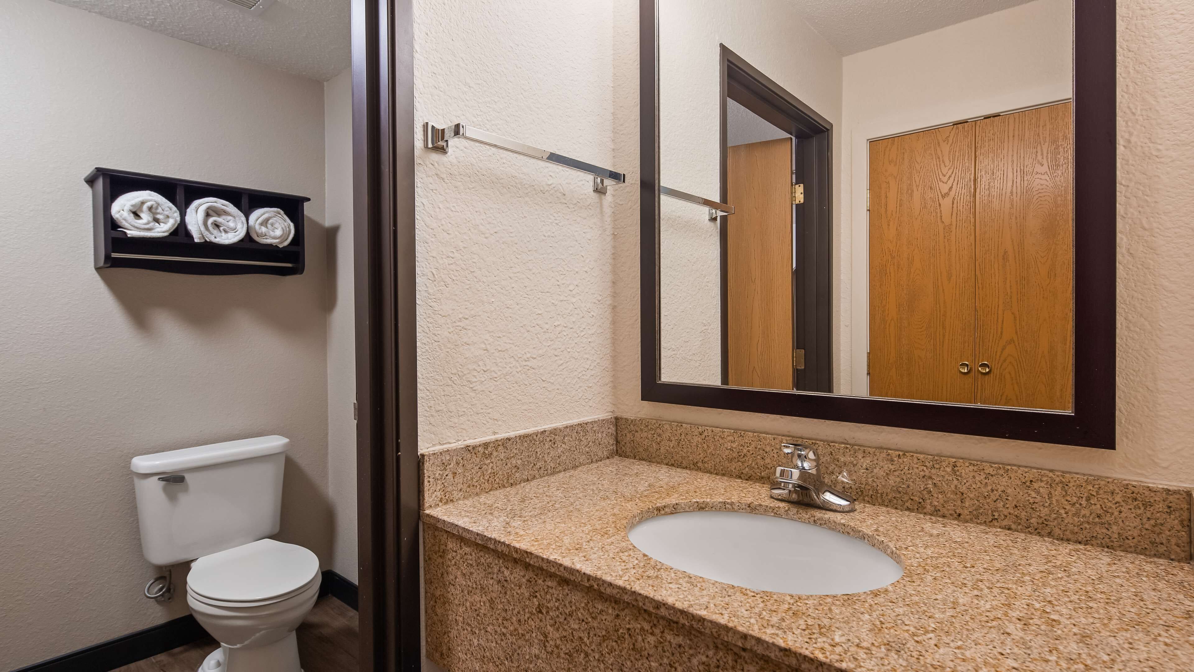 A bathroom with a white toilet, a granite countertop sink, a mirror, and a towel rack with towels.